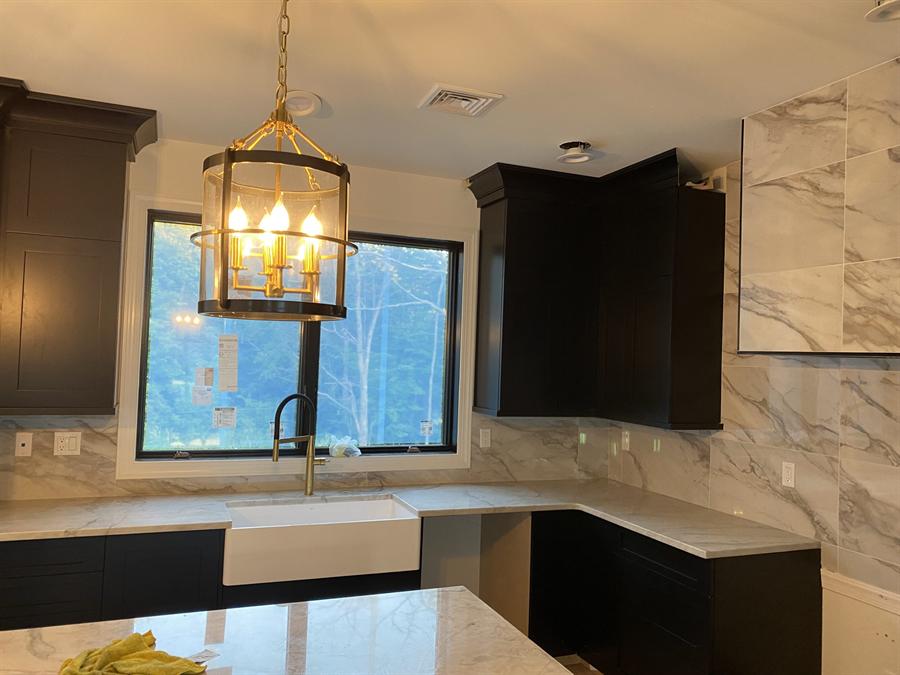 Dark cabinet kitchen with veined marble backsplash and brass pendant, New Jersey